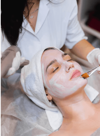 Woman receiving a facial treatment with a brush, while wrapped in a towel.