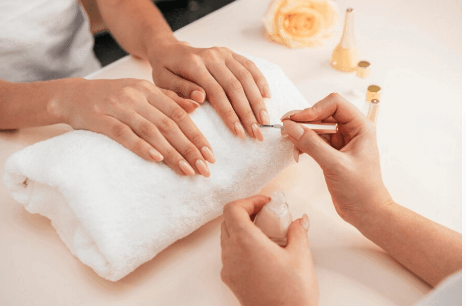 Person receiving a manicure with a white towel, rose, and nail polish bottles on table.